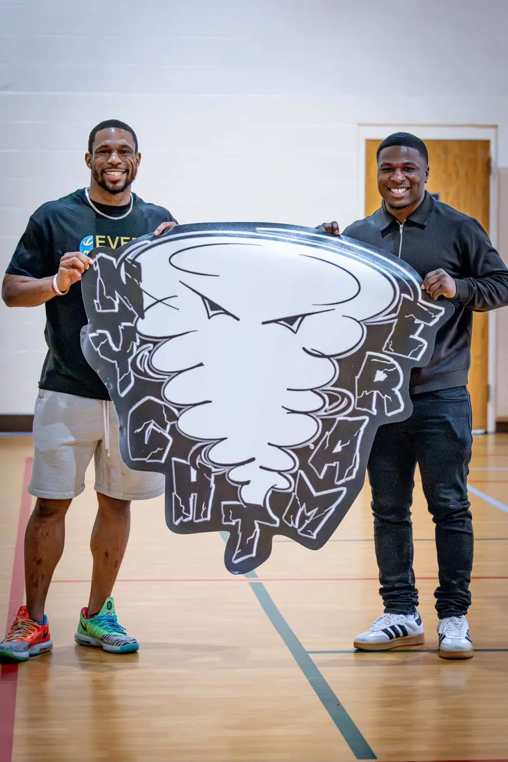 Two men holding a school mascot cutout in a gymnasium