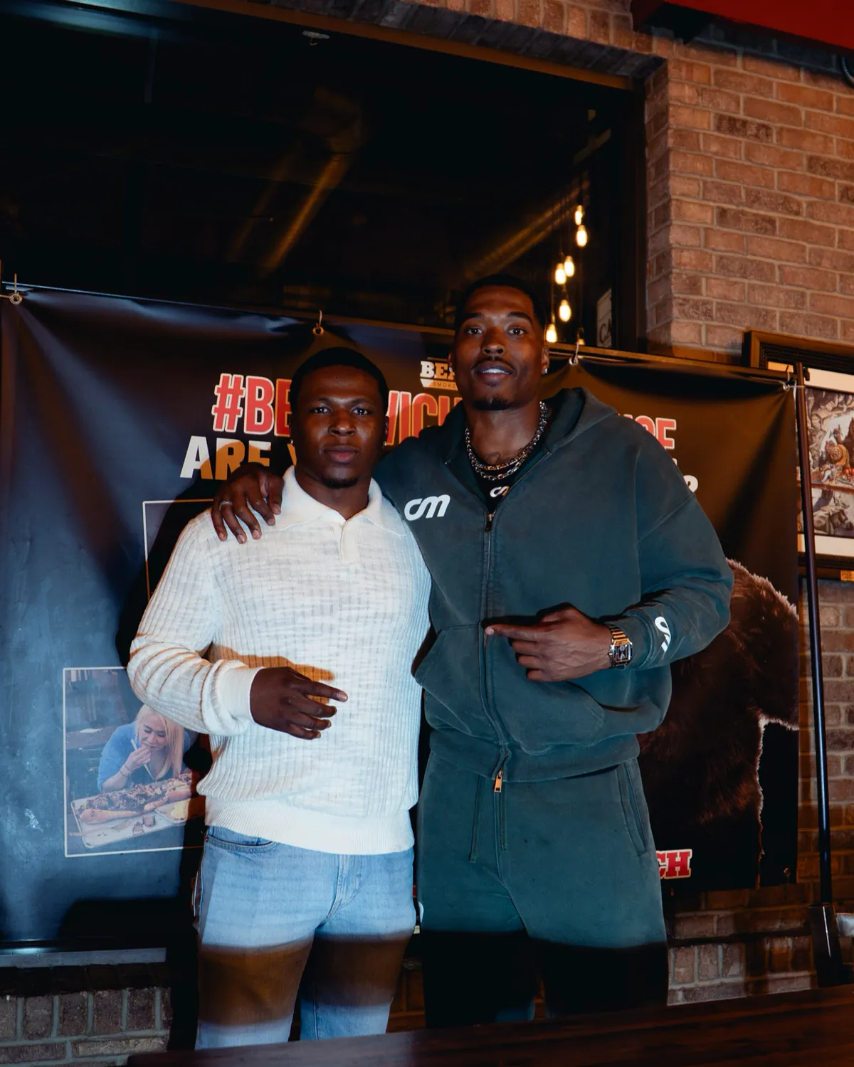 Two men at a brand event in front of a sponsor banner