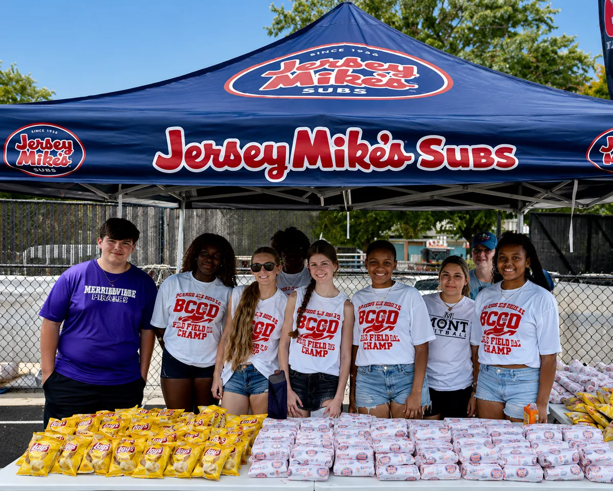 Volunteers serving food under a Jersey Mike's Subs tent at a community field day